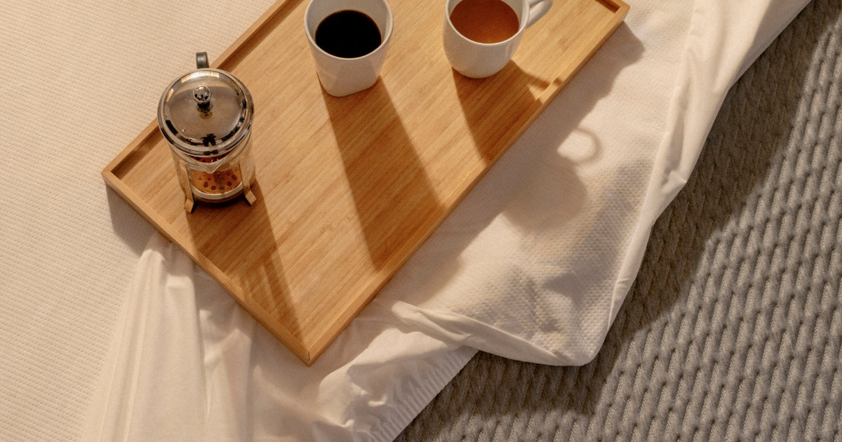 Wood tray with coffee and tea in white mugs sitting on top of a Tuft and Needle mattress