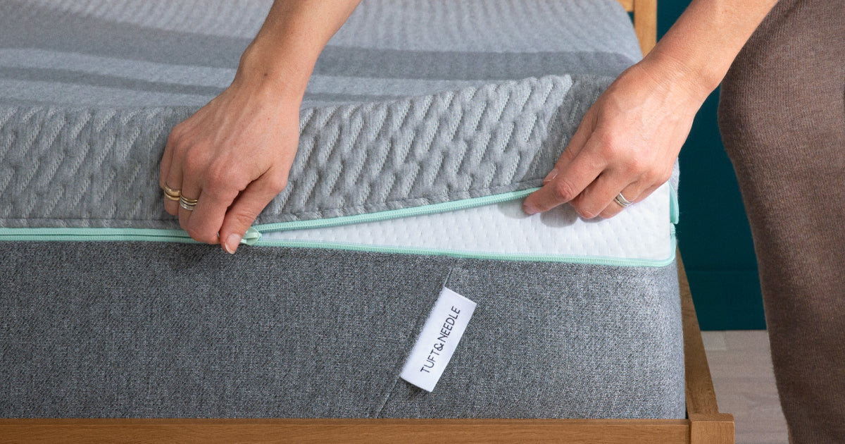 Two hands showing how the Tuft & Needle Mint mattress cover can be unzipped so it can be washed