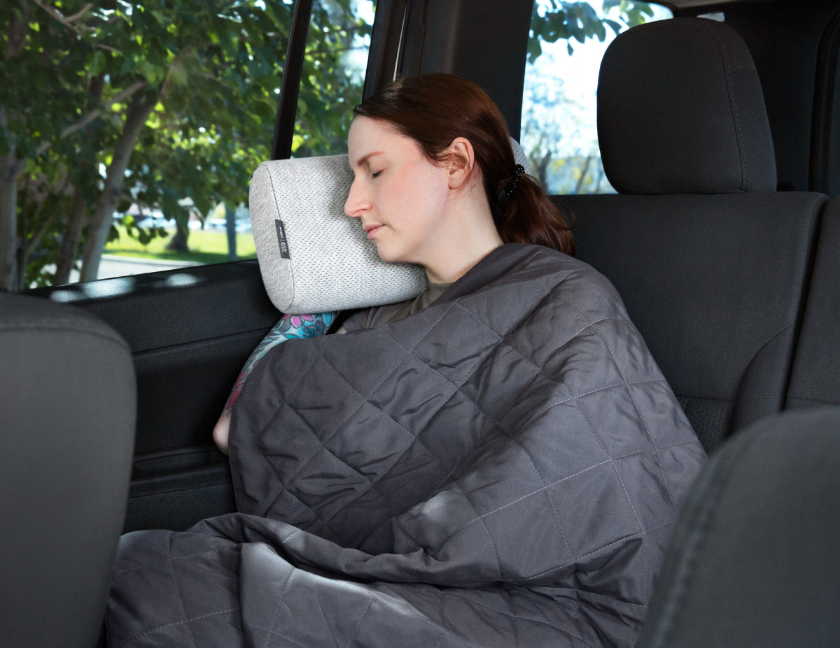 Woman sleeping in a car with the Tuft & Needle Travel Pillow and Blanket