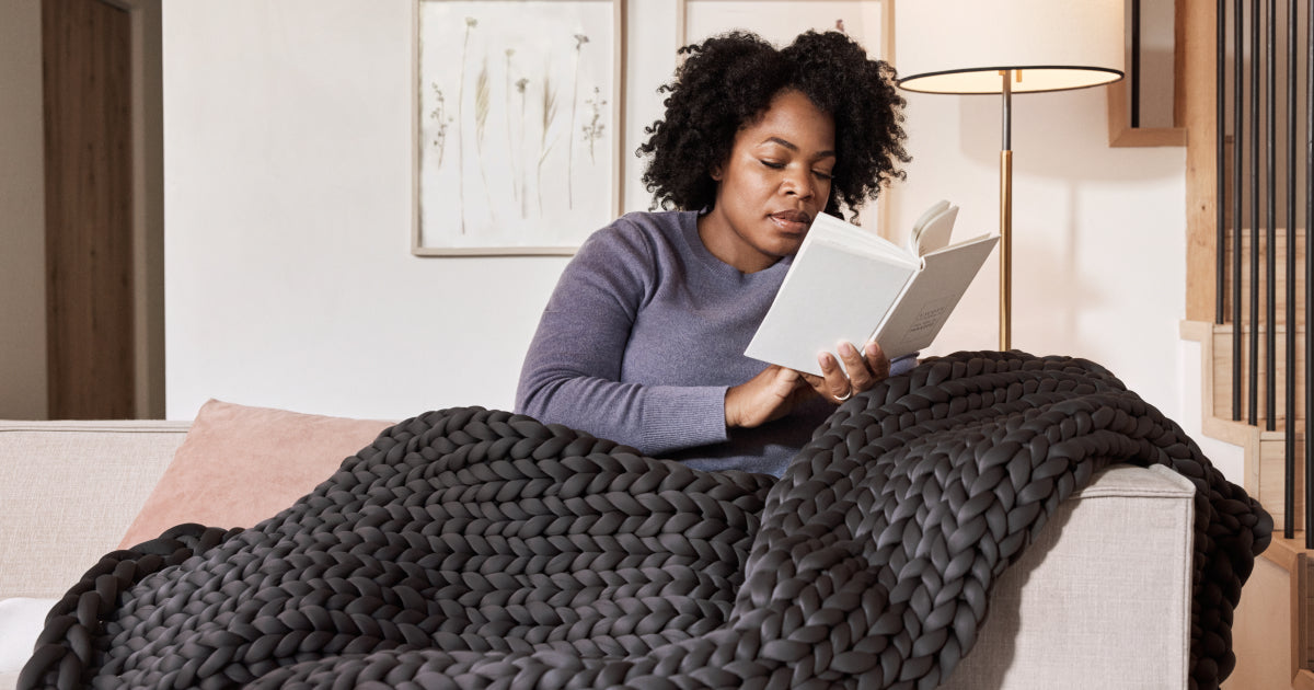 Woman reading a book on a couch with the Tuft & Needle weighted blanket on her lap