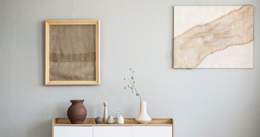 A sideboard with a picture frame and canvas painting hung above it