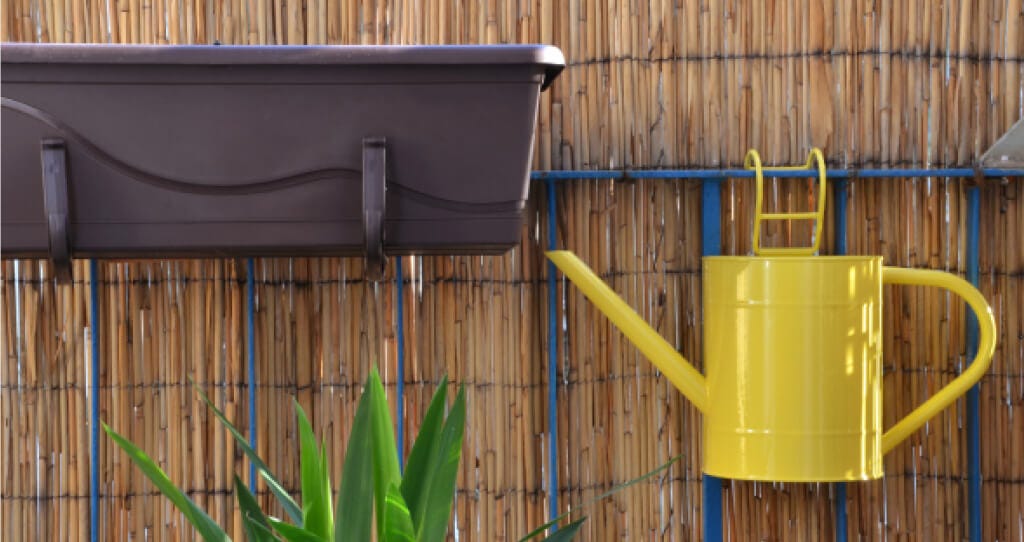 A hanging flower basket and watering can on a balcony