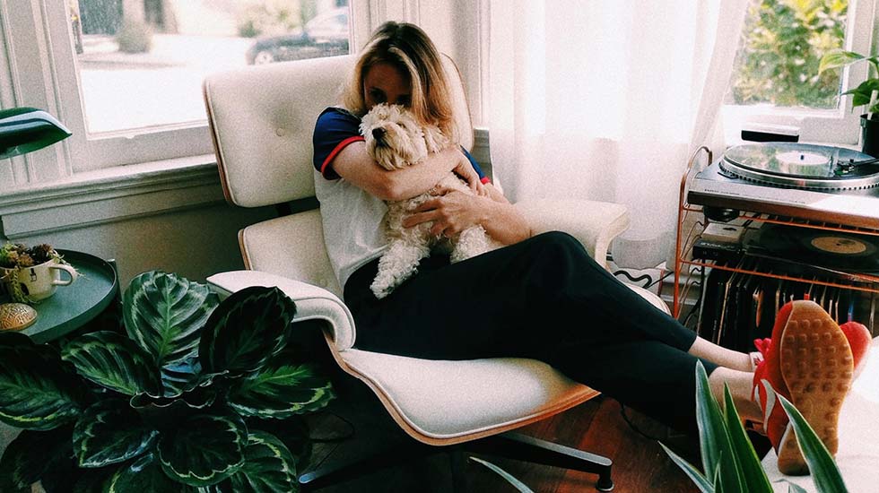 A woman holding a dog while sat on a chair surrounded by plants