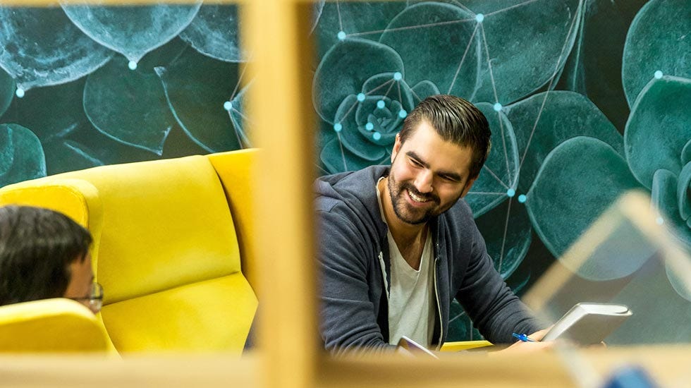 A man sitting on a yellow sofa, behind him is a wall covered in a plant print