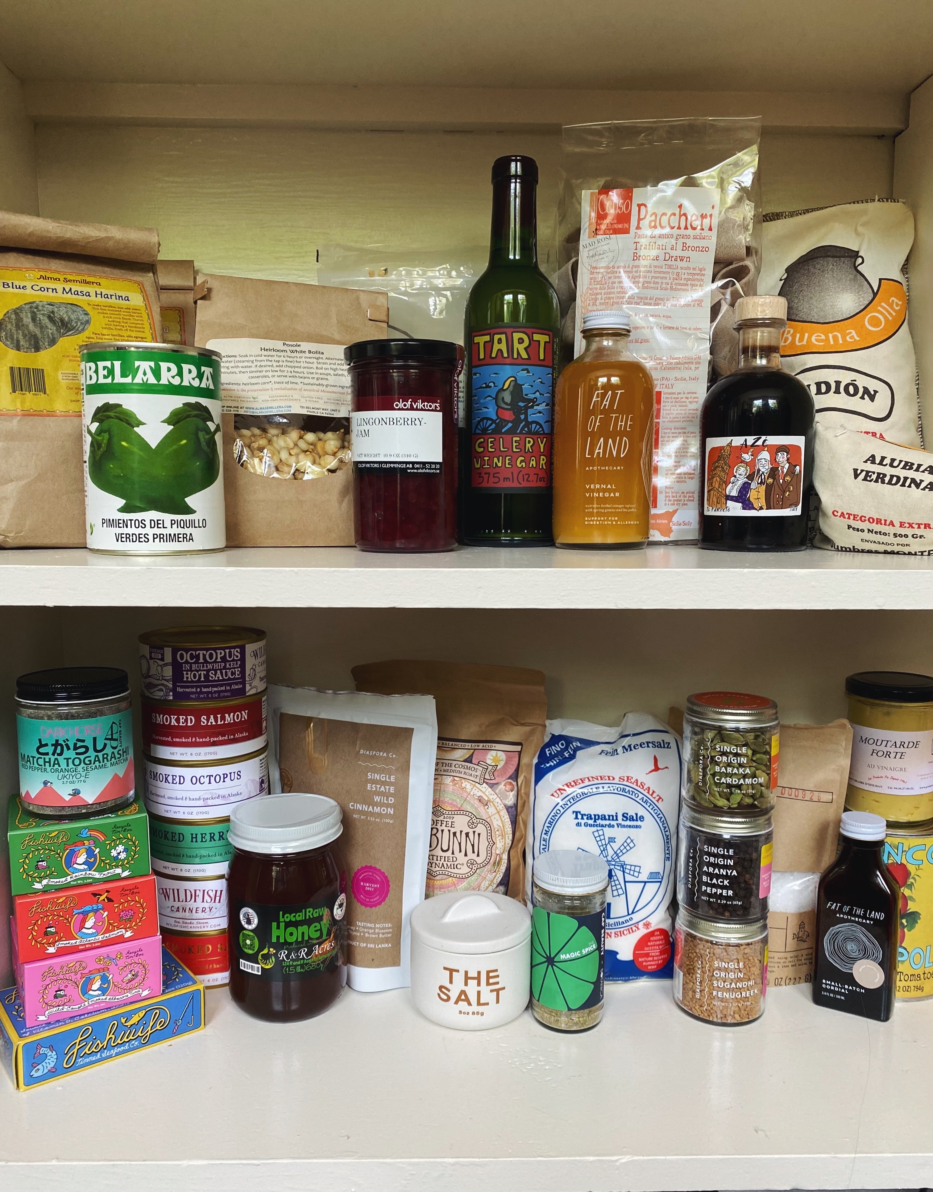 a kitchen cupboard featuring two shelves of miscelaneous specialty food jars and bottles