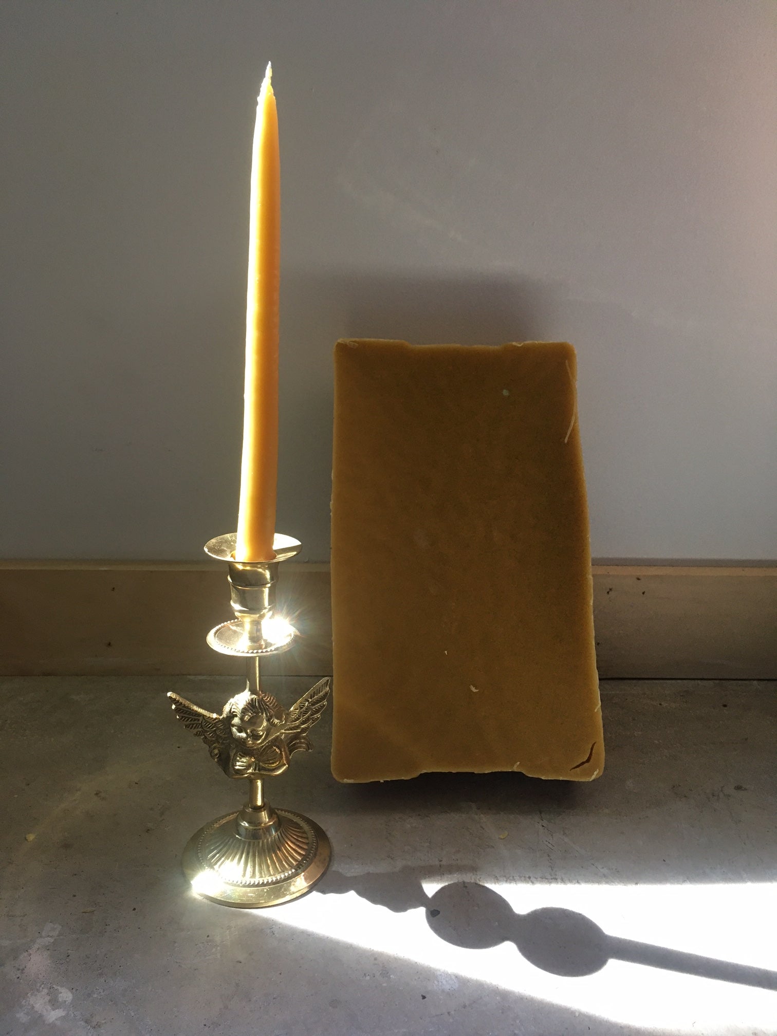 a beeswax candle sitting atop a candlestick, a block of beeswax in the background. 