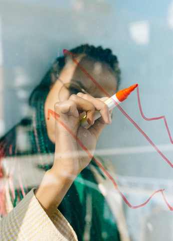 Women writing red arrows on transparent glass facing updwards to highlight growth or an increase