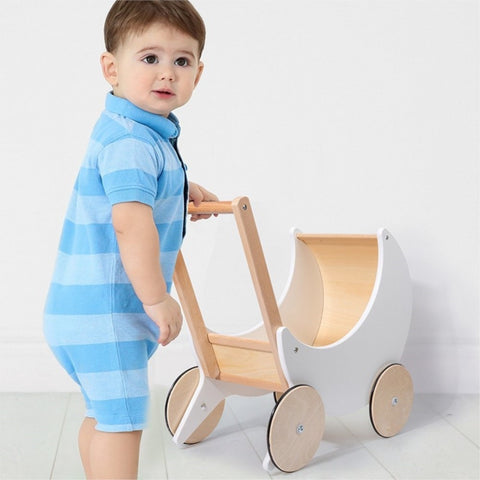 Little boy playing with new wooden children's pram stroller toy