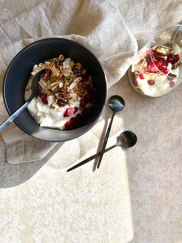 Date and sesame granola in a bowl with yoghurt and fruit beside a natural coloured napkin