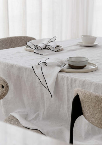 White linen napkin and tablecloth with embroidered black edging set on a table.