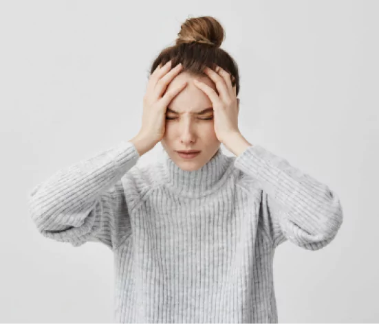 Woman in sweater with hands on head, looking stressed.