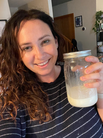 Curly-haired brunette smiling and holding up her first pint of goat's milk
