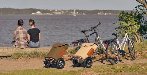 A young couple sitting by a lake with their bicycles and shopper trollies behind them on the shore