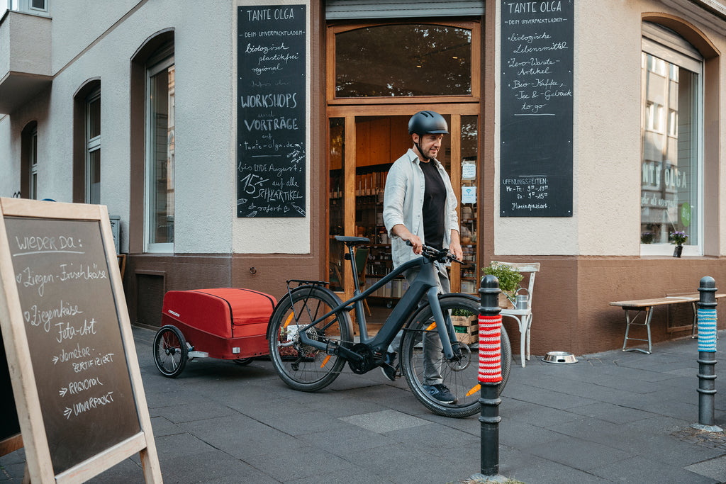 A man outside a shop with a bicycle towing a Croozer Cargo trailer