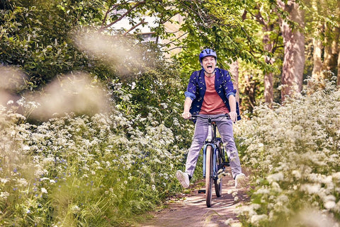 A man on a bicycle on a woodland path wearing a Raleigh cycle helmet