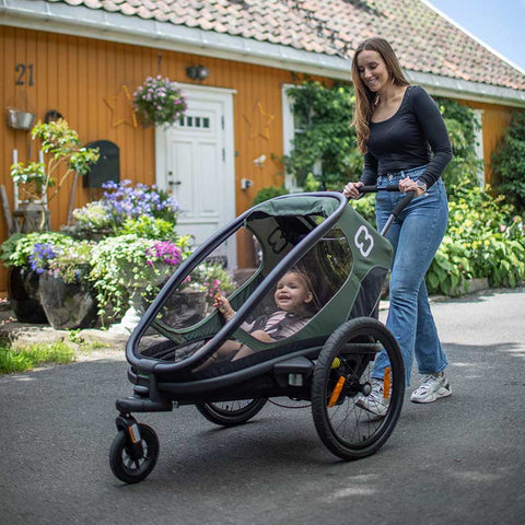 A woman pushing her child in a Hamax Outback trailer