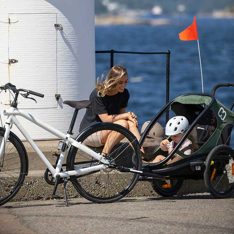 A woman sitting on the sidewalk with her child in a Hamax Outback trailer