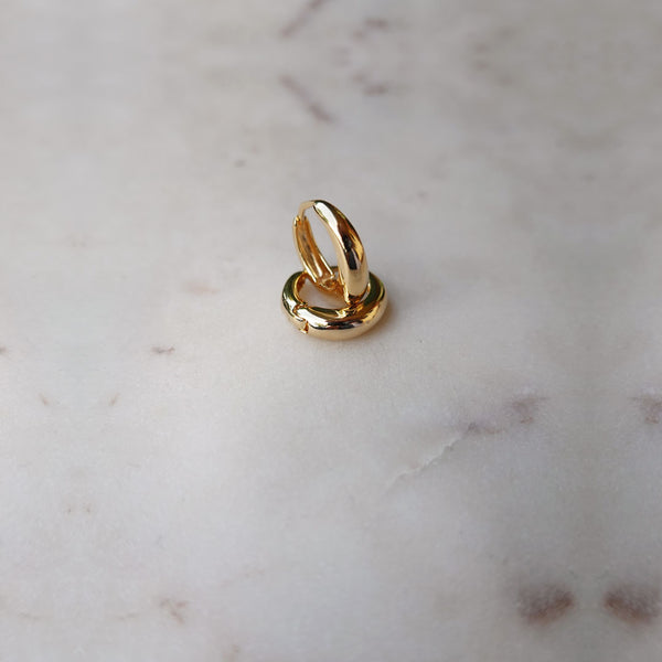 Dome gold filled hoop earrings stacked on top of each other, on a piece of marble.
