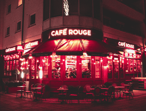 an inward looking view of the outside of a small cafe, illuminated by red neon signage lighting