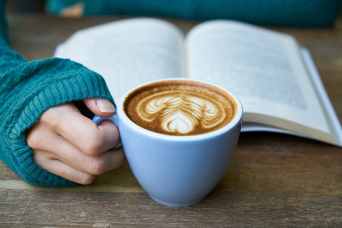 A hand holding a cup of coffee with a Bible next to it image for Coffee and Christ blog by Coffee and Christ Shop