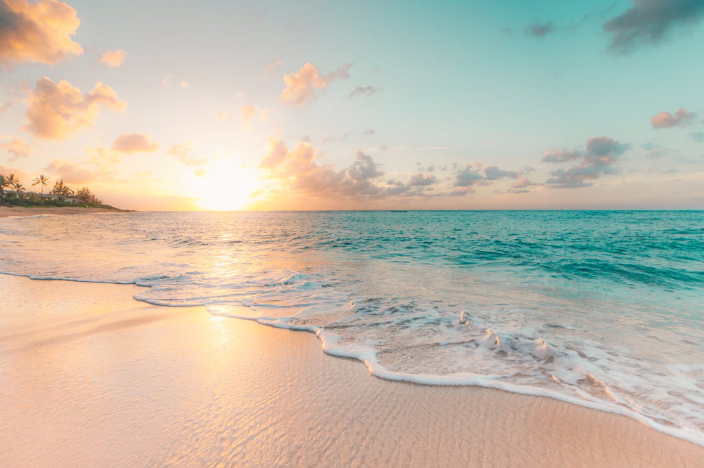 A serene and stunning image of the Jamaican coastline at sunset, featuring light sand, gentle waves, and a pastel colour palette.