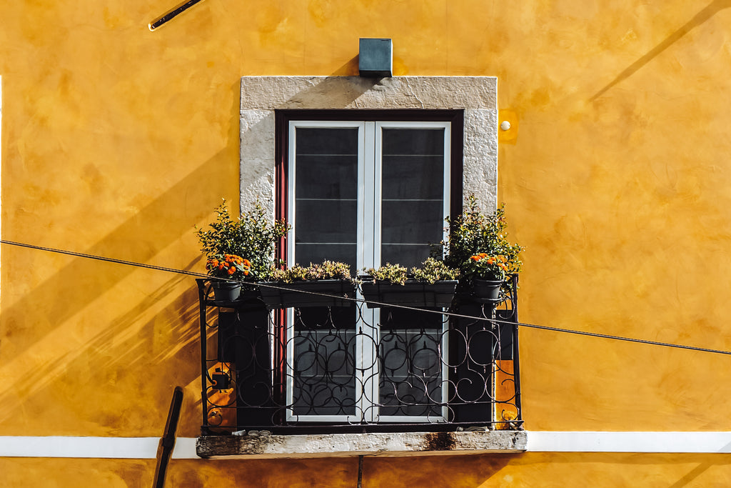 Image of a traditional Portuguese yellow building with a romantic balcony adorned with plants and flowers.