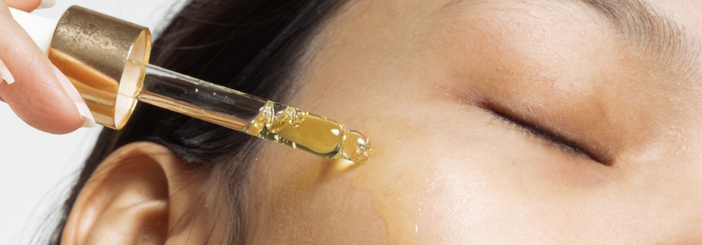 En kvinna droppar olja från en pipett på kinden.