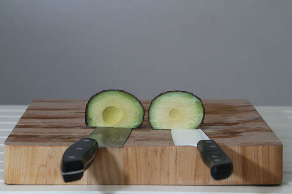 A ceramic knife and a stainless steel knife cutting an avocado to show a comparison between the materials.