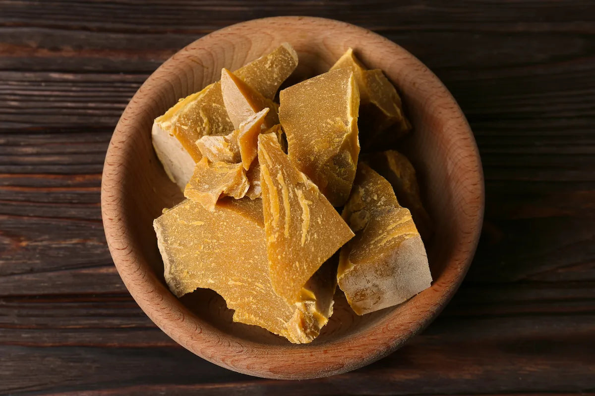 Raw beeswax chunks in wooden bowl, showcasing natural wax used in cosmetics and skincare