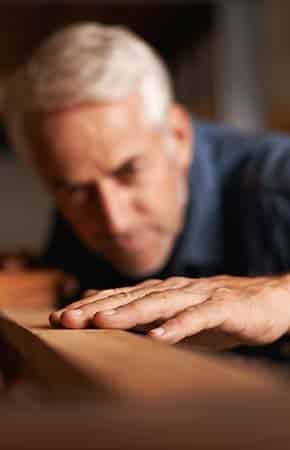 Man doing wood work running hand over wood. Supple Drink with chondroitin. Tip: strengthening hands helps with hand pain.