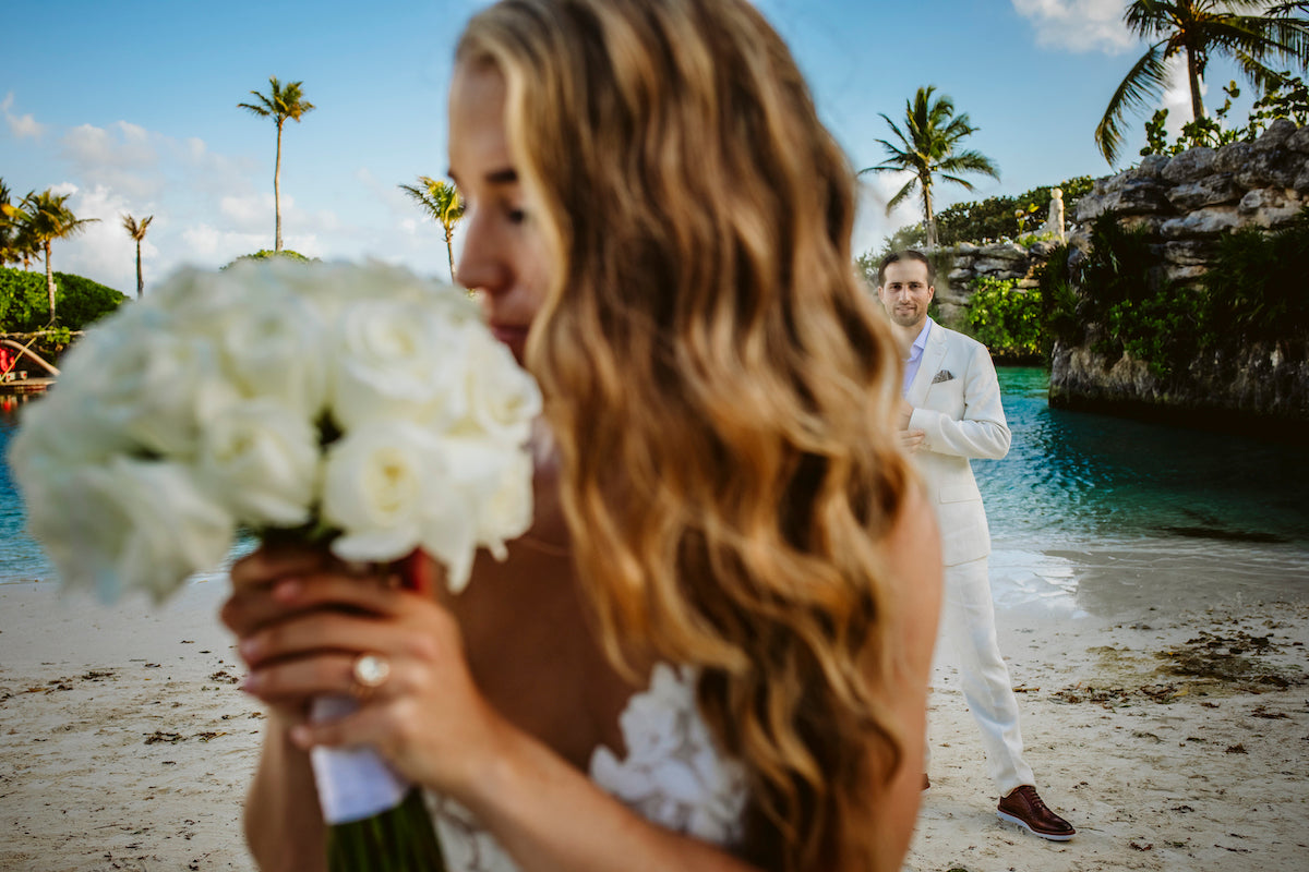 Bride holding her bouquet with groom in the background