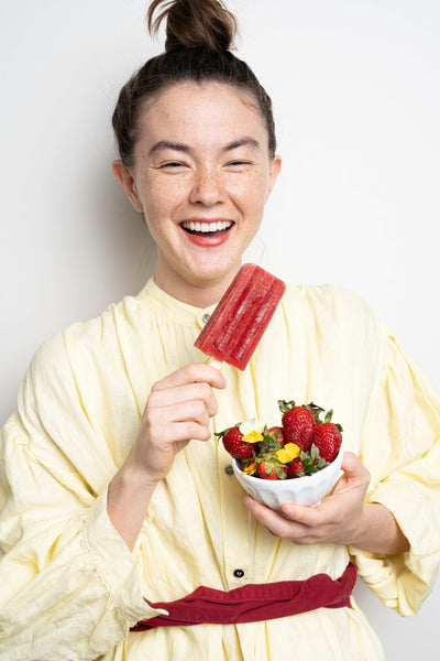 A girl holding a red strawberry ice pop and a bowl of strawberries.