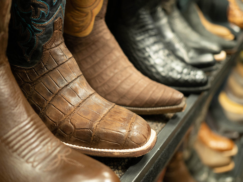 Several pairs of various colored cowboy boots sitting on a shelf for customer display