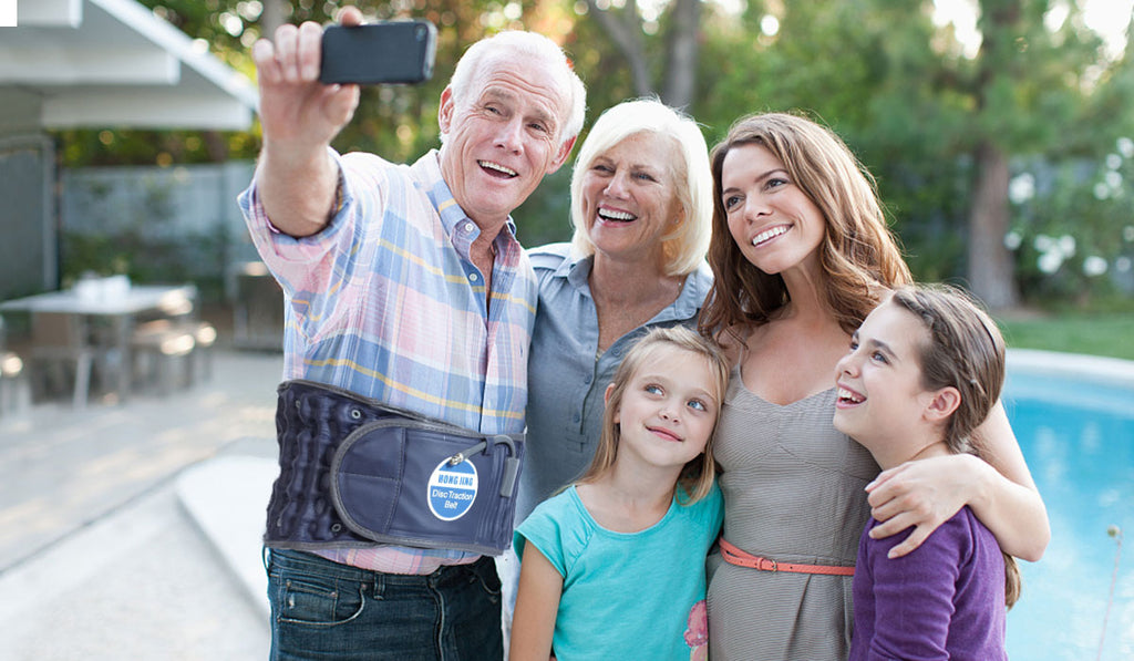 An elderly man takes a photo with his family wearing a decompression back belt
