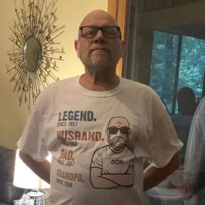 A man standing indoors wearing a t-shirt with the text 'LEGEND, HUSBAND, DAD, GRANDPA' and a graphic.