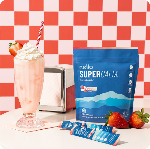 Strawberry milkshake and Nello Super Calm drink mix on table with red checkered background.