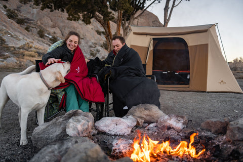 A couple sits with their dogs in front of a TETON Sports Mesa Canvas Tent on a cold morning.