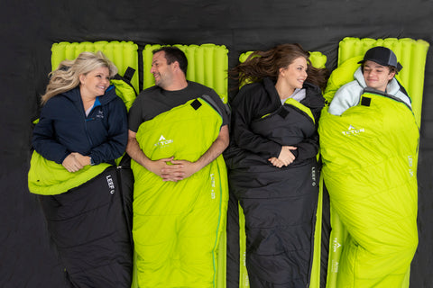 Four people are snuggled into TETON Sports LEEF Sleeping Bags and lying atop Altos Inflatable Camp Pads.