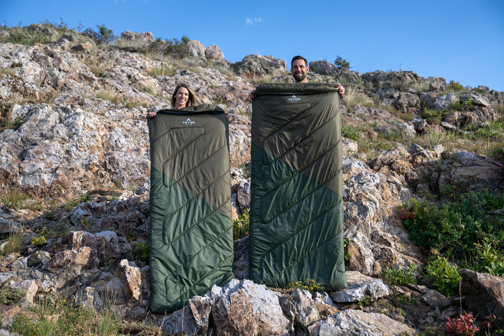 Man and woman hold up two sleeping bags.