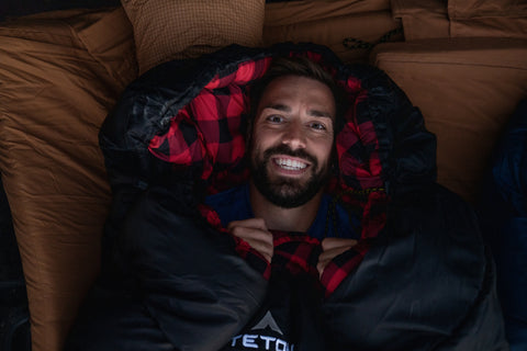 A man smiles at the camera while snuggled up in a TETON Sports Celsius XXL Sleeping Bag.