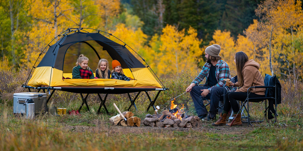 Family camps together around fire in field in the fall.