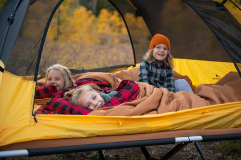 Three children snuggle together within a TETON Sports Vista Tent using their Deer Hunter Canvas Sleeping Bags.