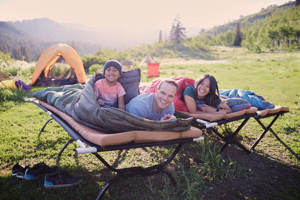 Family lays on cots and smiles at camp site.