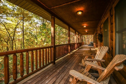 A log cabin front porch with wooden seating in an autumn forest.