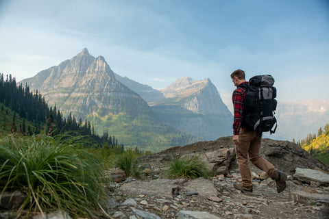 A lone backpacker ascends a small, rocky hill with mountains in the background.