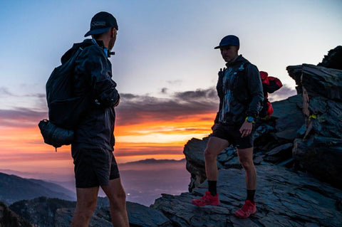 Two backpackers talking by a ledge overlooking a gorgeous sunset.