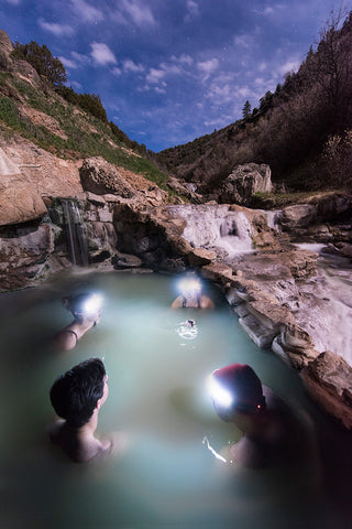 People sit inside natural hot springs together at dusk.