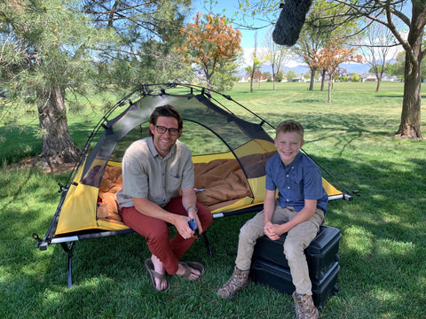 A man and a young boy sit together in front of a TETON Sports Vista Tent in yellow.