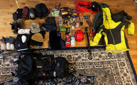 Backpacking items lying together on a wooden floor and rug, ready to be packed into a backpack.