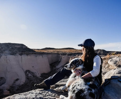 A woman and her dog seated on a ledge by a canyon.
